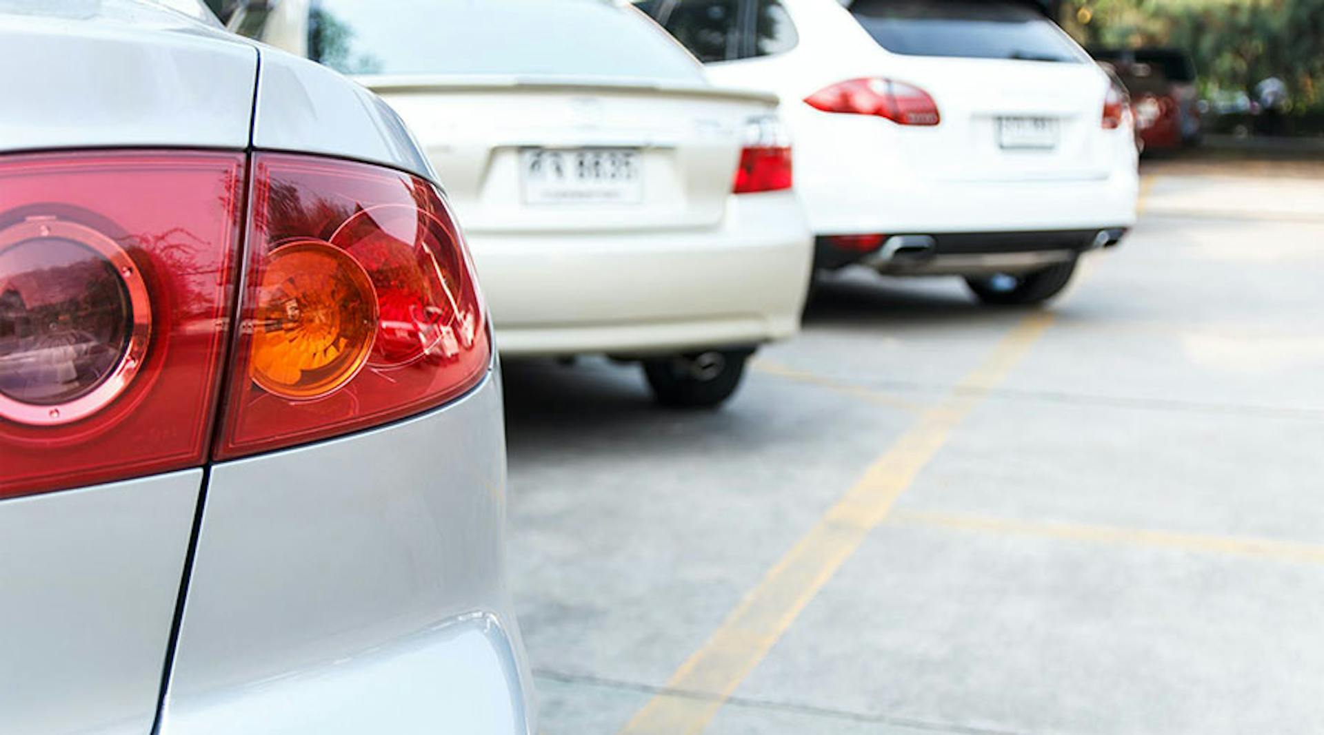 An close focus shot of the rear taillight of a car, parked in an outdoor lot. Two more cars are parked next to it.