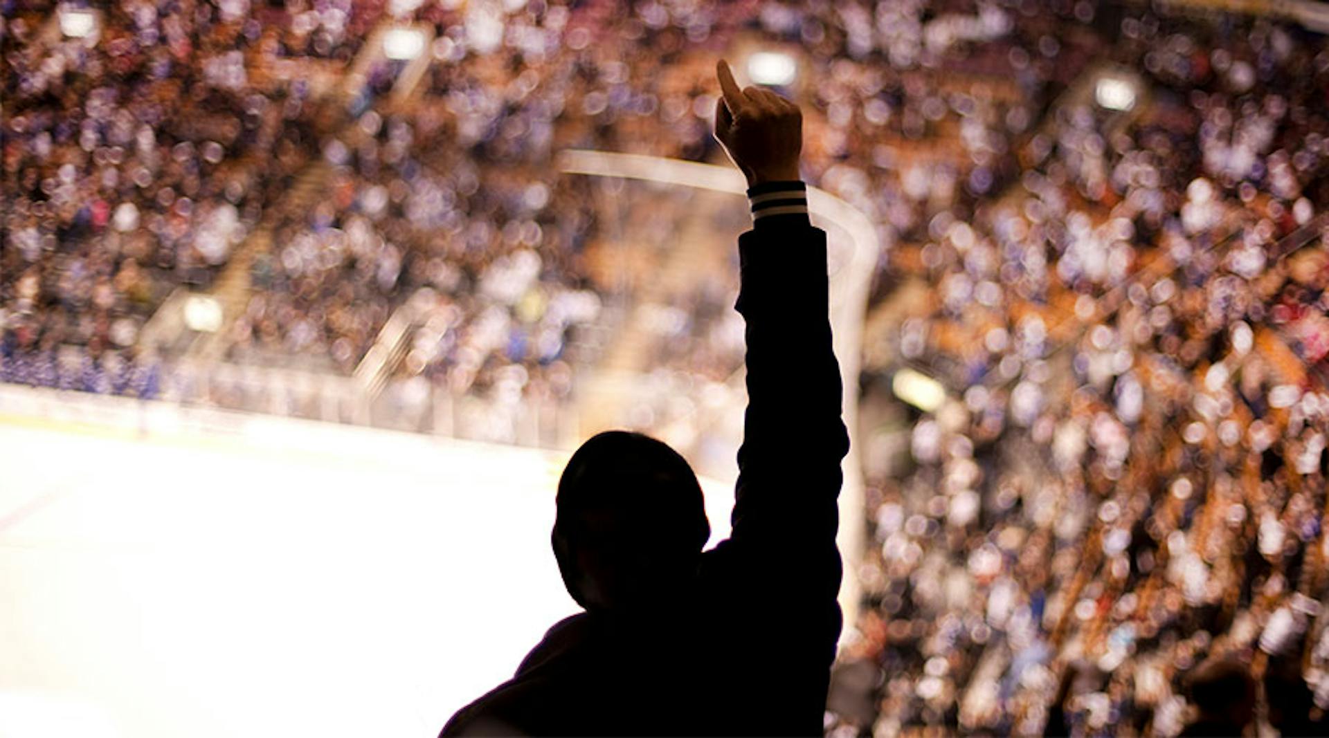 The silhouette of a person with their arm raised in triumph while in the crowd at a sports arena